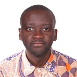 A young Black man wearing a bright orange and purple patterned shirt looks serious