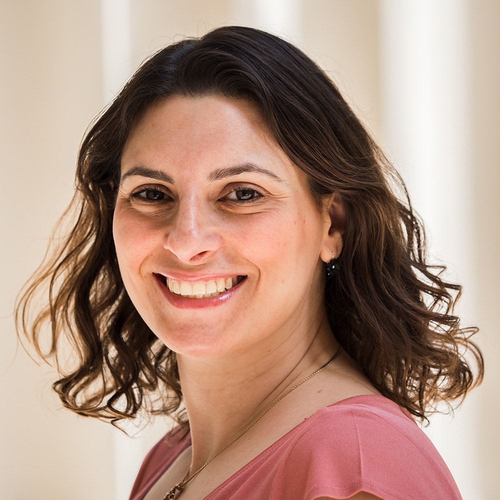 A young white woman with short brown curls gives a sunny smile