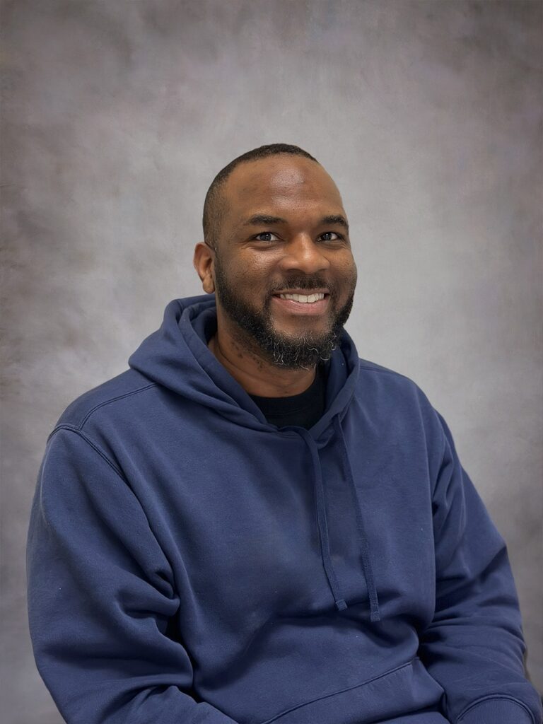 A younger Black man smiles from his office