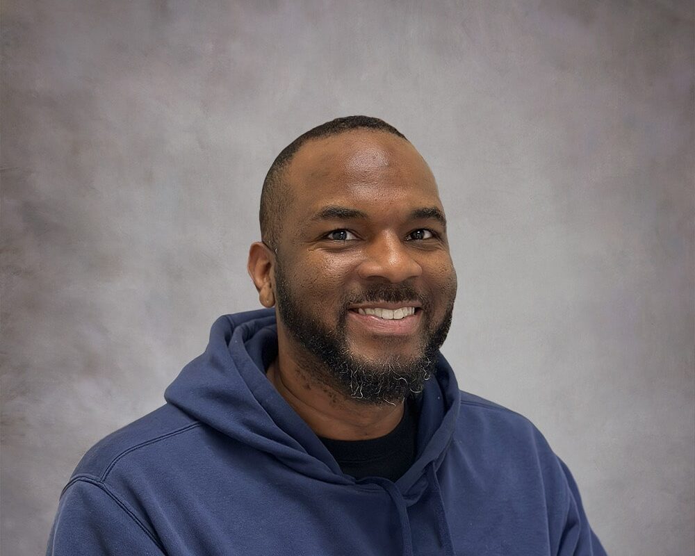 A younger Black man smiles from his office