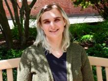 A young white woman with bleached hair smiles from an outdoor bench